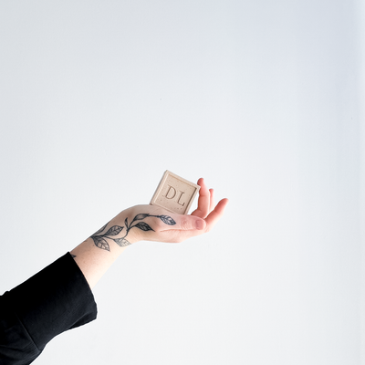 Hand holding a vegan soap with 'DL' initials against a white background