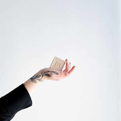 Hand holding a vegan soap with 'DL' initials against a white background