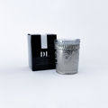 Silver candle holder with decorative design next to a black box with 'DL' branding on a white background