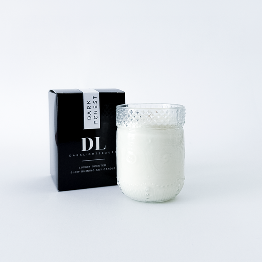 White candle in a textured glass holder with a black box labeled 'Dark Forest' on a white background