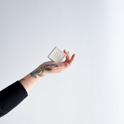 Hand holding a vegan soap with 'DL' on a light gray background