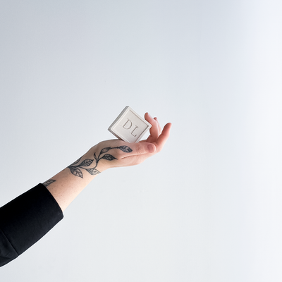 Hand holding a vegan soap with 'DL' on a light gray background