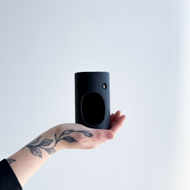 Hand holding a black ceramic oil burner  object against a light gray background