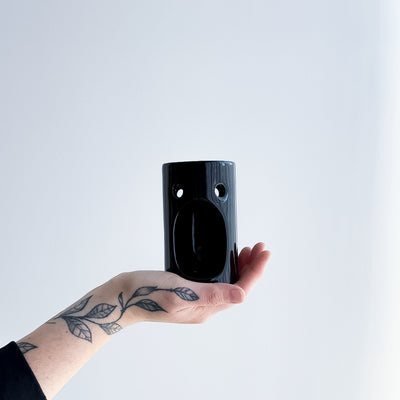 Hand holding a black ceramic oil burner  against a light gray background