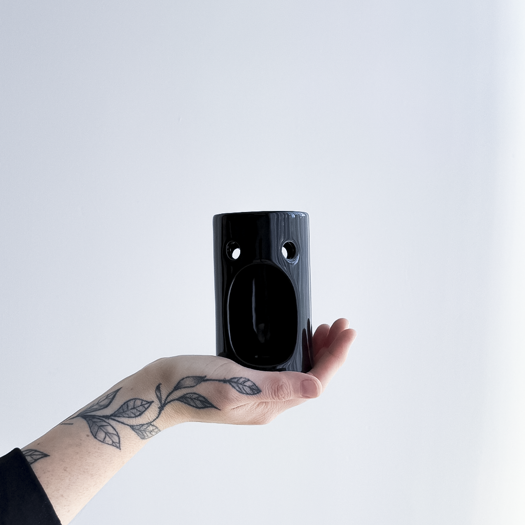 Hand holding a black ceramic oil burner  against a light gray background