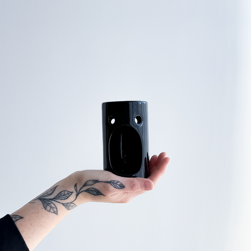 Hand holding a black ceramic oil burner  against a light gray background