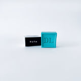 Two small rectangular boxes, one black with 'RUTH' and one blue with 'DL', on a light gray background.