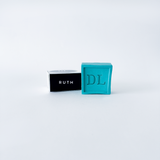 Two small rectangular boxes, one black with 'RUTH' and one blue with 'DL', on a light gray background.