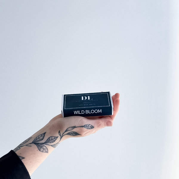 Hand holding a box labeled 'Wild Bloom' with 'DL' branding on a light gray background