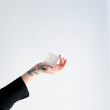 Hand holding a small rectangular object with 'DL' on it against a white background