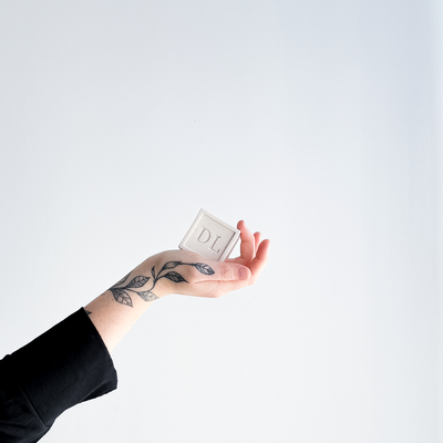 Hand holding a small rectangular object with 'DL' on it against a white background