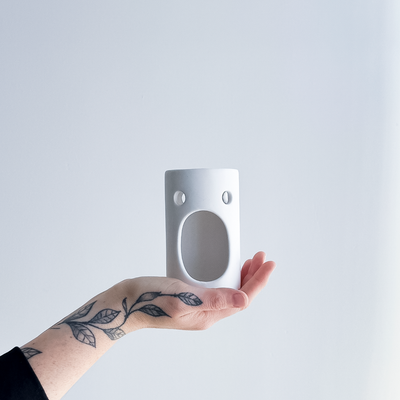 Hand holding a white ceramic burner with a plain background