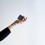Hand holding a black soap with 'DL' branding against a white background