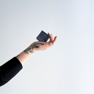 Hand holding a black soap with 'DL' branding against a white background